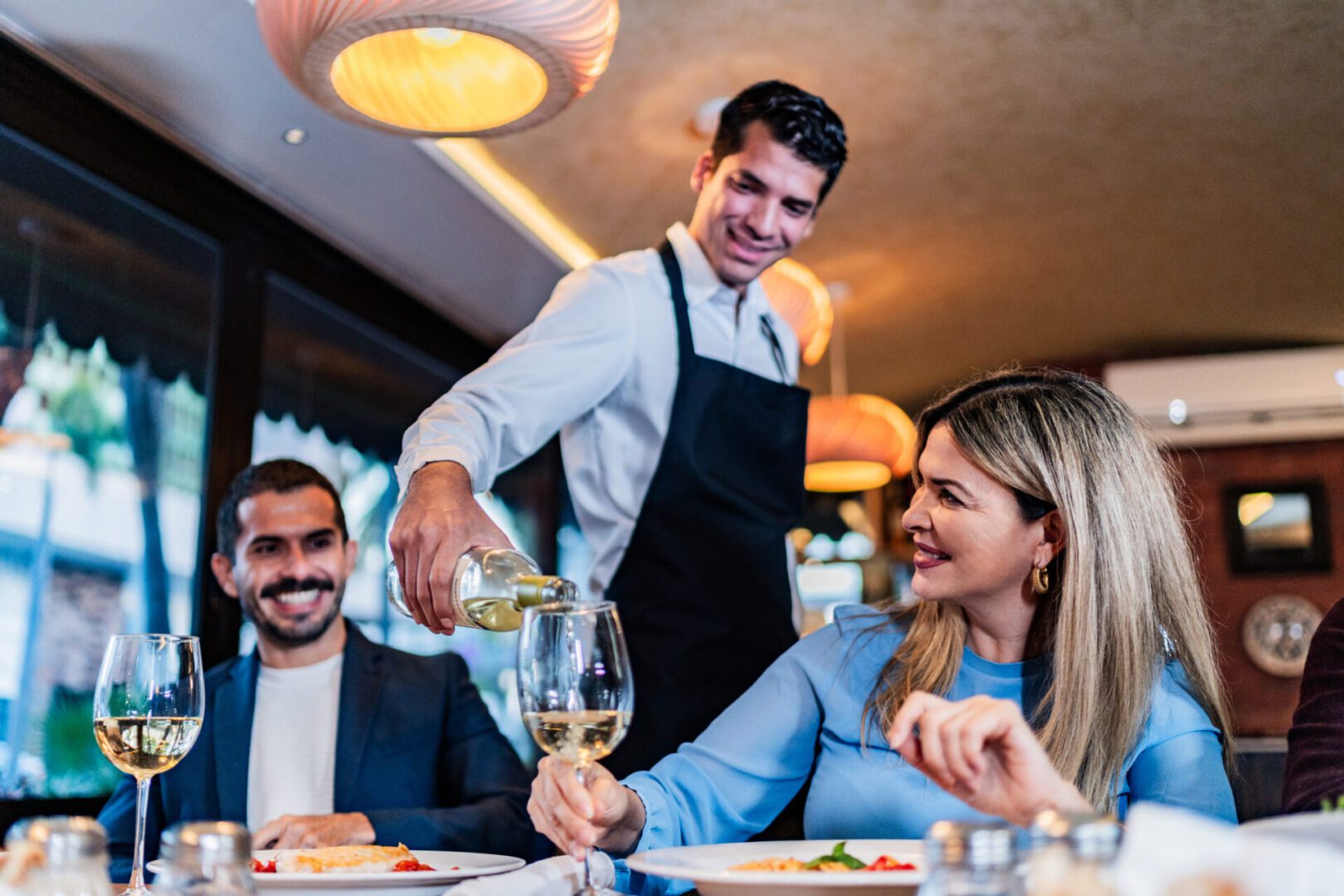 Waiter pouring wine for smiling diners